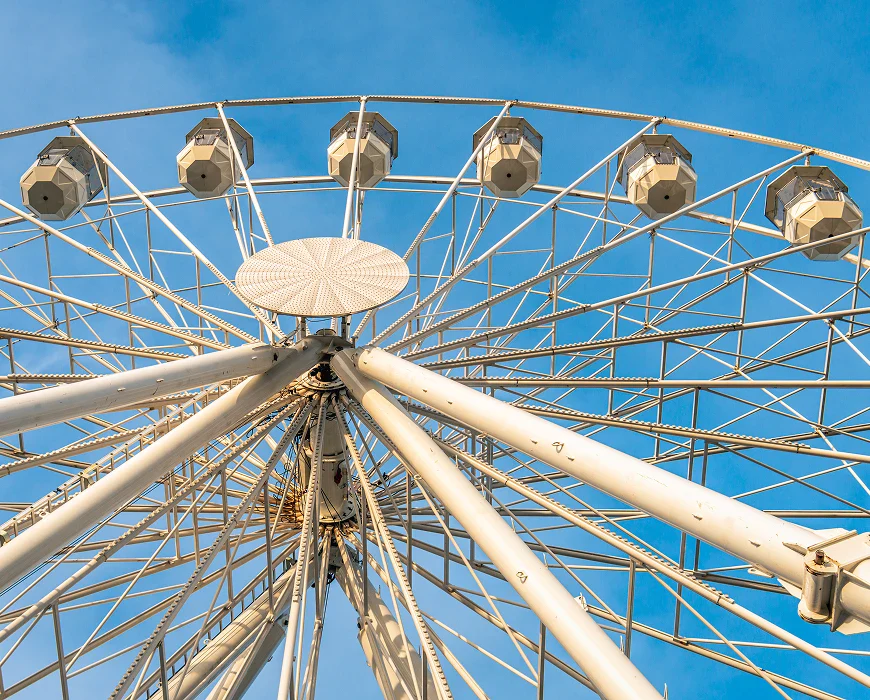 A close-up view of a ferris wheel's structure against a clear blue sky, showcasing its metal frame and passenger cabins.